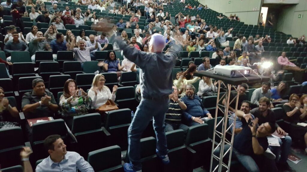 Empolgação na palestra, pisando somente nos braços da cadeira. Haja equilíbrio no entusiasmo!